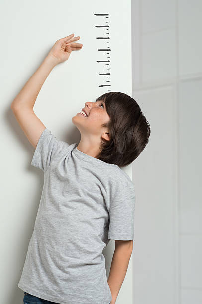 Boy measuring his height Closeup of little boy measuring height himself against white wall. Smiling cute boy measures his height. Boy growing tall. Young boy checking his height with the hand. meter instrument of measurement photos stock pictures, royalty-free photos & images