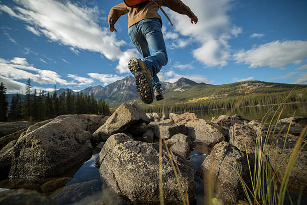 Hiker jumps rock to rock in mountain lake. Low angle