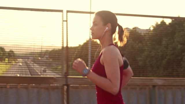SLO MO Woman jogging across a highway overpass in sunset