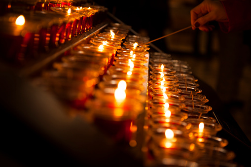 Spirituality.  One man lighting a red candle in a Catholic church chapel in New York City, USA.  The glowing candles are lined up in a row. Diminishing perspective.  The candles serve as a vigil or spiritual prayer.  Reverence, hope, religion.    