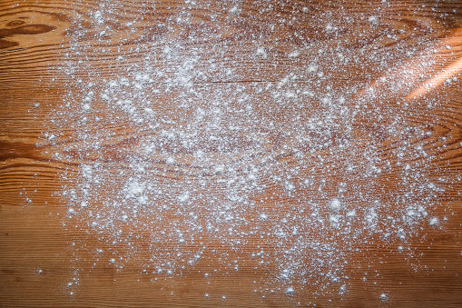White flour scattered on rustic wooden board with ray of sunlight coming from side. Baking background.