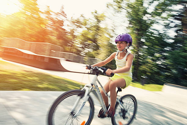Little girl aged 9 riding her bicycle in the park. Panning shot, Sunny summer day. A ramp is visible in the background. 