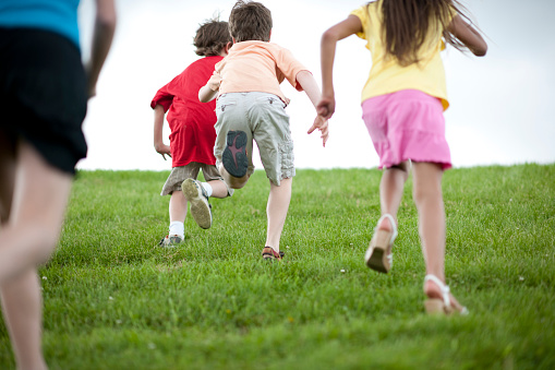 A multi-ethnic group of elementary age children are playing tag and chasing each other up a hill.