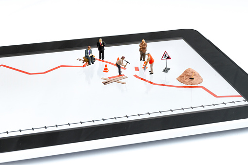 Digital tablet with broken graph and miniature of businessmen, consultant  (sitting on wheelbarrow) and workers that trying to repair a finance problem