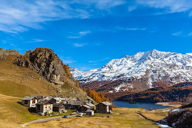 Stunning view of the Village Grevasalvas with the Sils lake, the swiss alps and golden trees in background, Upper Engadine in autumn, Canton of Grisons, Switzerland.