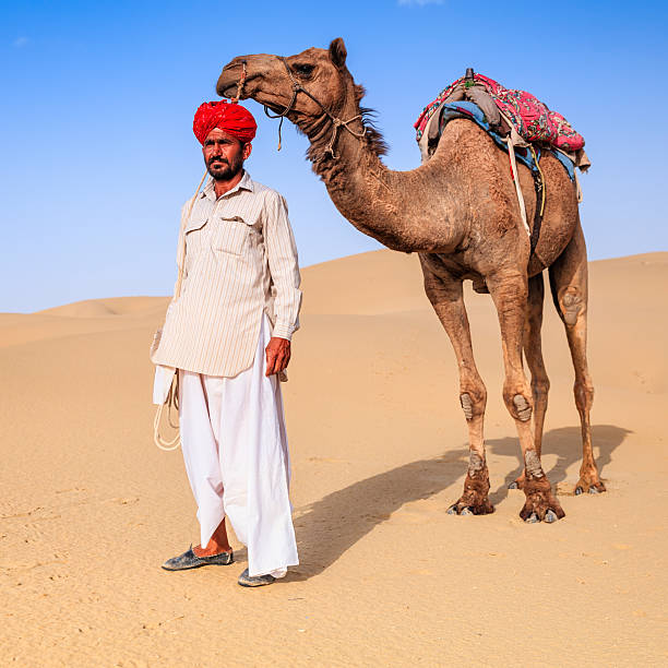 istock Indian man holding camel on sand dunes, Rajasthan, India 496353642