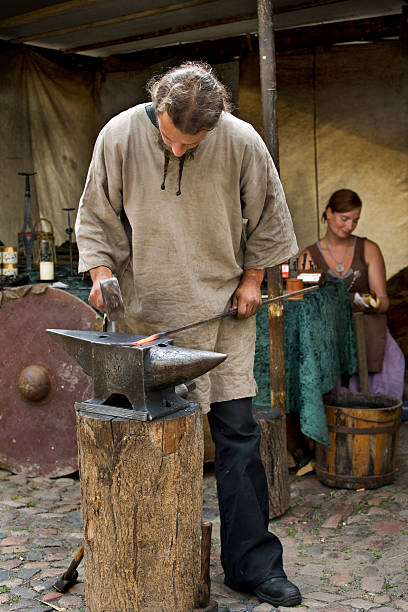 Torgau, Germany - June 14, 2014: Blacksmith with hammer and anvil at work on medieval market. Couple in medieval clothing showing the lifestyle of common people in this time period.