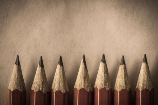 A row of red pencils with tips facing upwards aganst parchment textured paper which provides copy space above. Processed in a retro or vintage style.