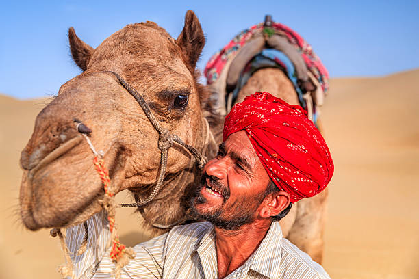 istock Indian man holding camel on sand dunes, Rajasthan, India 496356324