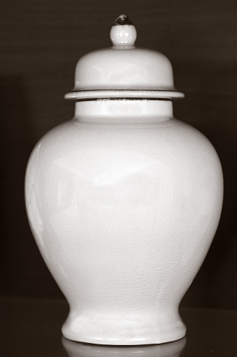 White funeral urn jar shape complete view isolated on dark wooden background.Philosophical concept photo of life ,death, cremation, reincarnation, spiritual , religious , soul ,spirit and spirality