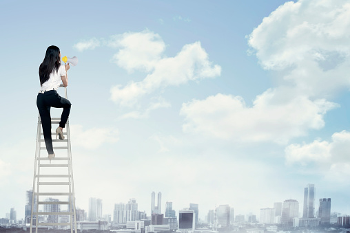 Business woman standing on the ladder high and shout with megaphone. Leadership concept