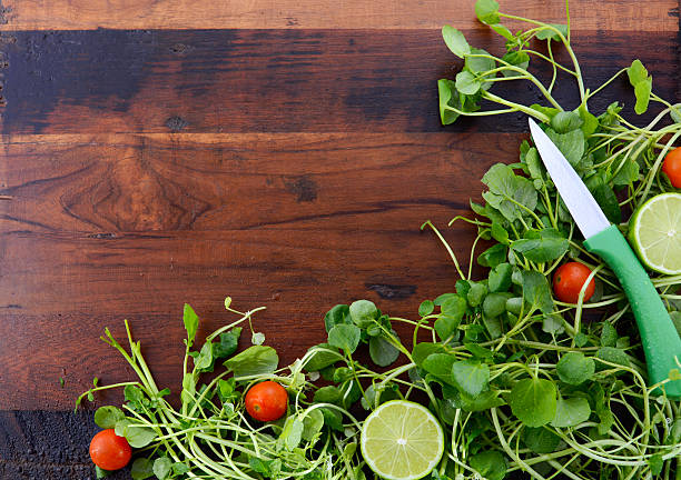 Salad Preparation with fresh watercess, cherry tomatoes and limes on dark wood rustic table with copy space.