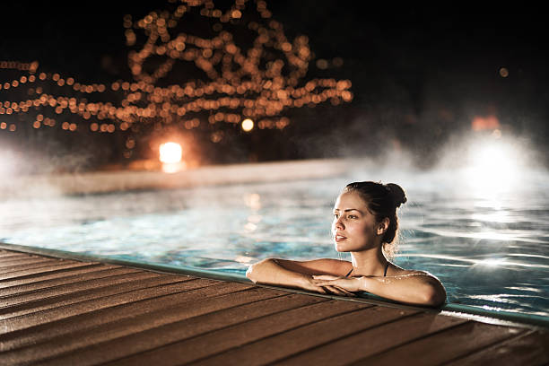 jeune femme de se détendre dans la piscine chauffée en hiver nuit. - hot spring photos et images de collection