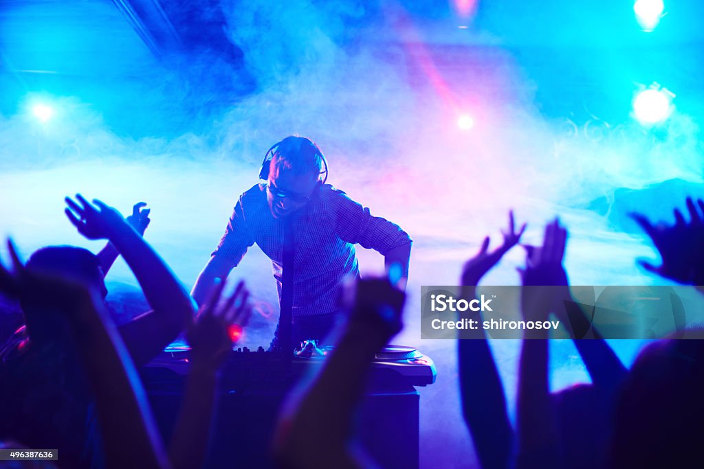 Deejay in club Energetic deejay standing in front of dancing people in club DJ Stock Photo