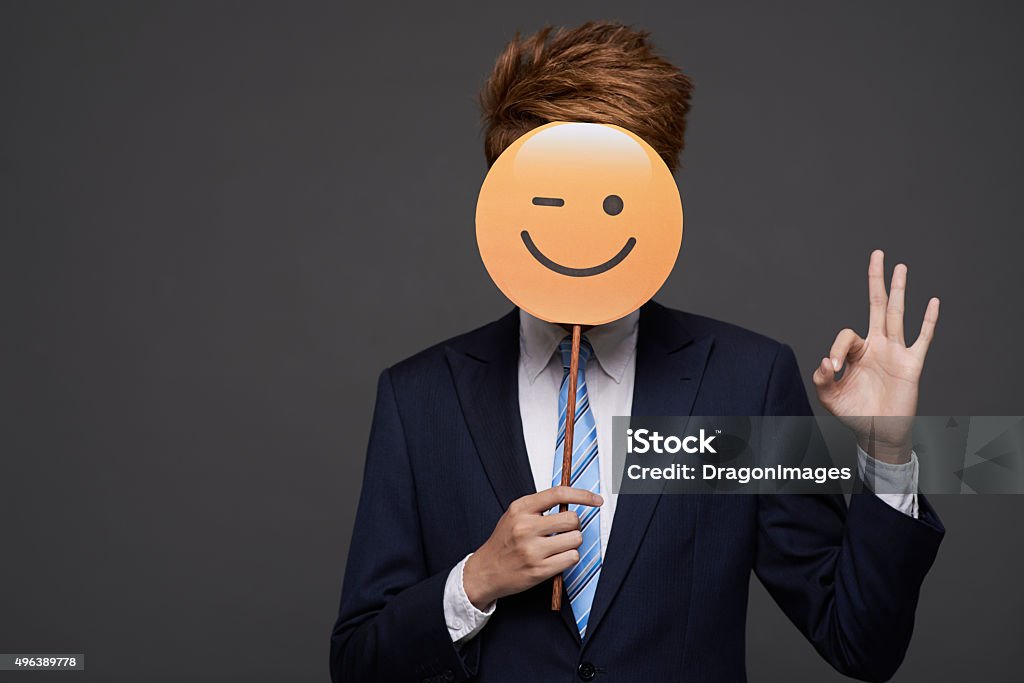 Winking face Businessman showing ok sign and covering head with winking face Emoticon Stock Photo