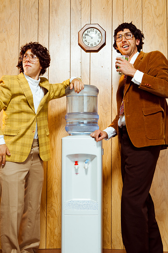 Two retro office nerds by the water cooler. Concept shot in stdio with wood panelling background.