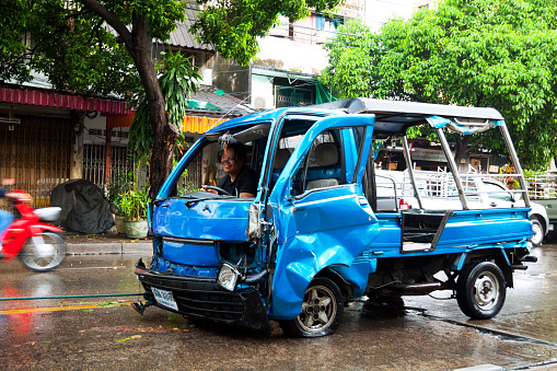 Bangkok, Thailand - May 6, 2014: Capture of crashed and damaged blue local tuk-tuk taxi in street Chokchai 4 after heavy rain, Street is wet. Driver is sitting in tuk-tuk and happy smiling. Tuk-tuk is pulled by other car, connected by rope.