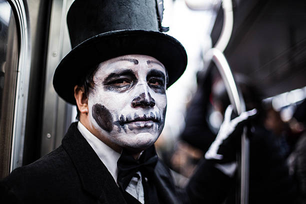 New York City, NY, USA - October 31, 2015: Man dressed in suit and top hat with Día de Muertos / sugar skull face paint, on the train, heading downtown. Halloween night.