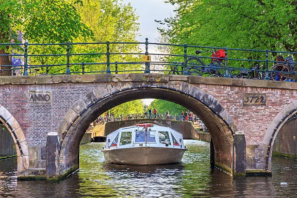 Canal cruise boat goes under the bridge over the Leidse canal at the Patricians' or Lords' canal (Herengracht) in Amsterdam in spring