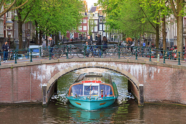 Amsterdam, The Netherlands - May 2, 2014: Canal cruise boat with tourists goes under a bridge over the Leidse canal at the Emperors canal (Keizersgracht) in Amsterdam, The Netherlands, May 2, 2014
