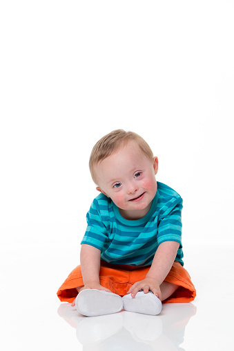 Portrait of a beautiful downsyndrome baby  boy sitting up against a white background.