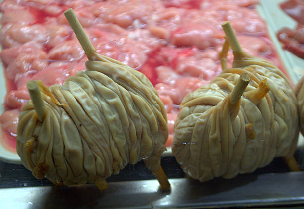 In the foreground rolled lamb guts in cylindrical shape, sausage type; three light wood slats come out of the two sausages; On the bottom tray of sliced pink meat.