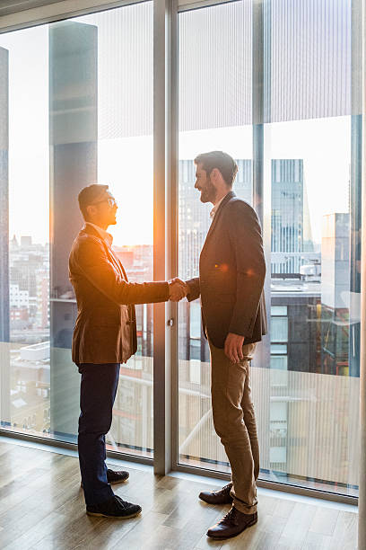 istock Businessmen shaking hands by modern office window 496440928