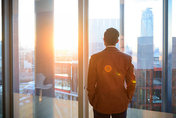 homme d'affaires, regardant par la fenêtre du bureau dans la lumière du soleil - business office business person window photos et images de collection