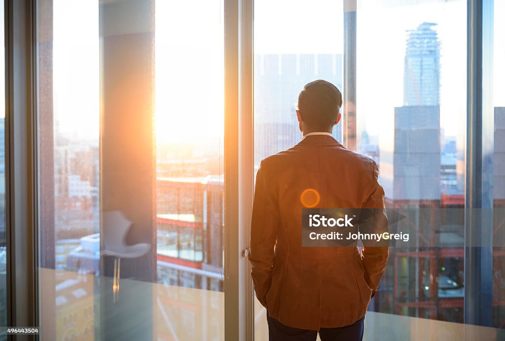 Businessman looking through office window in sunlight Male office worker looking at view through window of modern office over city. New beginnings, hope, the future. Man deep in contemplation. Change Stock Photo