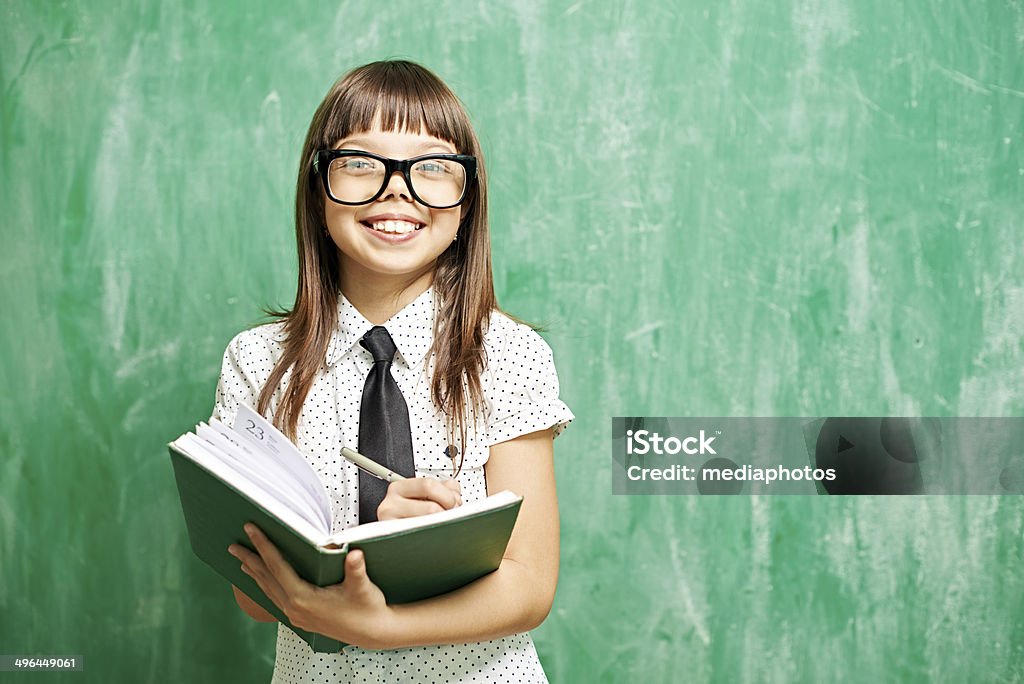 Love studying Cheerful little nerd writing in notebook standing against blackboard 8-9 Years Stock Photo
