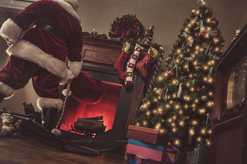 Christmas photo of an authentic Santa Claus climbing out of the fireplace in a family's living room to deliver presents.