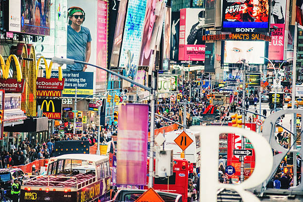 Young African American Man traveling in New York, wearing green short sleeve shirt, walking on busy street in Times Square of Manhattan, talking on cell phone. High buildings, cars on background.\