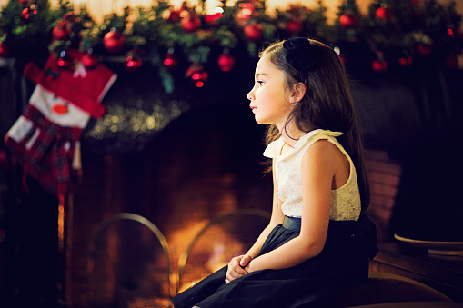 Little girl is waiting for Santa at the front of the fireplace.