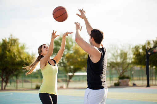 Cute brunette trying to score against her boyfriend on a friendly match on a basketball court