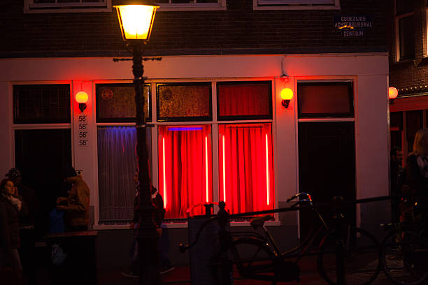 Red illuminated sex cabins Amsterdam, The Netherlands - October 2, 2015: Red illuminated sex cabins in Wallen of Amsterdam. Some people and tourists are walking along canal and sex cabins. wellen stock pictures, royalty-free photos & images