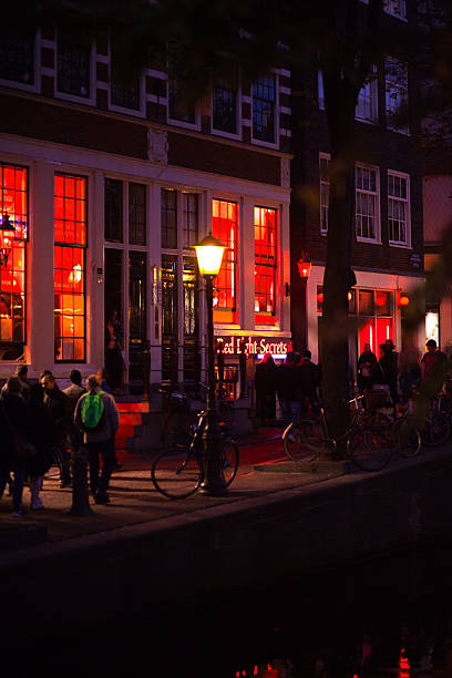 Tourists at Voorurgwal in night Amsterdam, The Netherlands - October 2, 2015: Capture of tourists walking along canal Voorburgwal in night. View over canal. In background red illuminated windows of prostitutes and two windows of Red Light Secrets museum of prostitution. wellen stock pictures, royalty-free photos & images