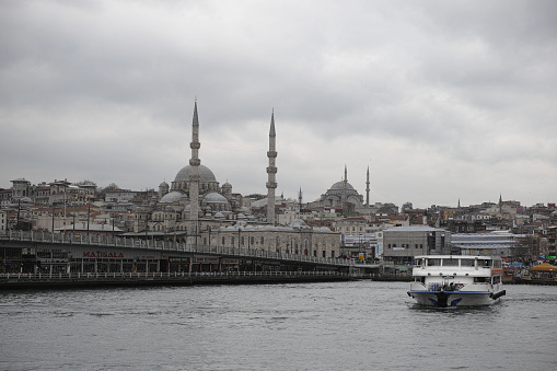 Istanbul, Turkey - September 30, 2015 A Mosque overlooks the Bosphorus Strait in istanbul the capital of Turkey. In the foreground people walk their way on Galata Bridge and ferrboat is leaving from Europa side to go Asia side, this image was taken on the ferryboat looking towards the European side.