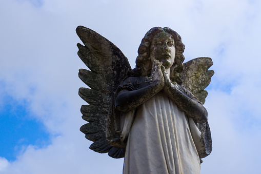 A peaceful image of a statue of an Angel Playing under Blue Cloudy Sky.
