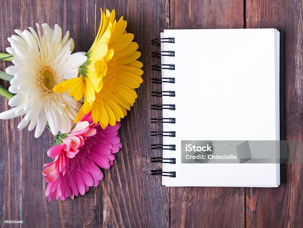 Gerbera flowers and notebook with blank page Three gerbera flowers and notebook with blank page on the wooden table, top view. 2015 Stock Photo