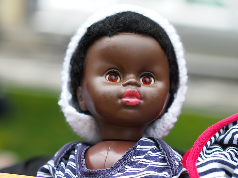 Little black color doll looking wide eyes open in white fut hat. 