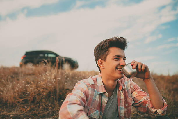 Smiling handsome teenage boy drinking tea Confident smiling teenage boy sitting outdoors by his suv car on background and drinking tea hipster car stock pictures, royalty-free photos & images