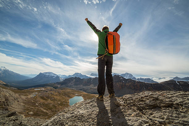 Young man hiking stands on a mountain top arms outstretched for freedom and positive emotion. Spectacular mountain and lake scenery.