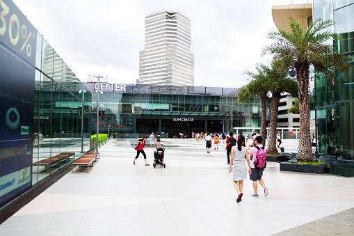 Bangkok, Thailand - July 16, 2013: Siam Center Mall in Bangkok seen from exit of BTS station Siam. View over square. Some people are walking over square. In background is a fountain on square.