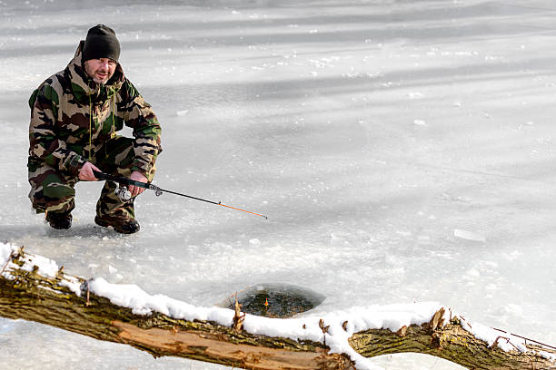 fishing in winter season fisherman in warm clothing fishing in ice lake. man ice fishing stock pictures, royalty-free photos & images