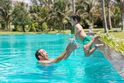 Man catching his son who is jumping into the pool