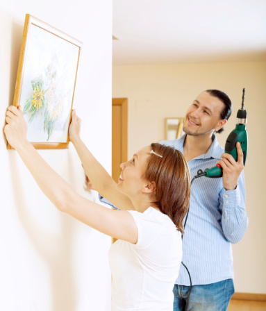 middle-aged man and woman  hanging  art picture in frame on wall at home interior