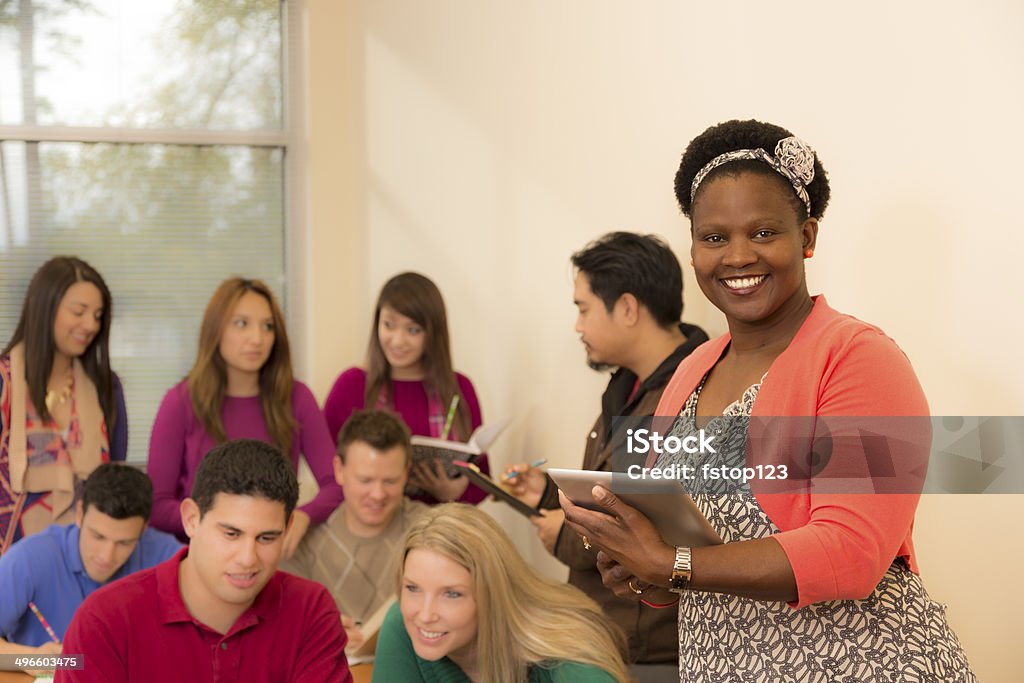 Education: Diverse college students, teacher in classroom. African descent college professor helps college students during class using digital tablet.  Mixed-aged students collaborate on project. African Ethnicity Stock Photo