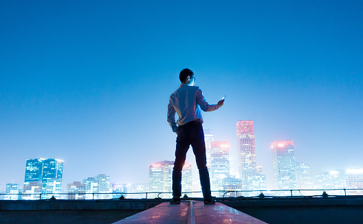 Businessman using smart phone standing on roof with city skyline,Beijing,China