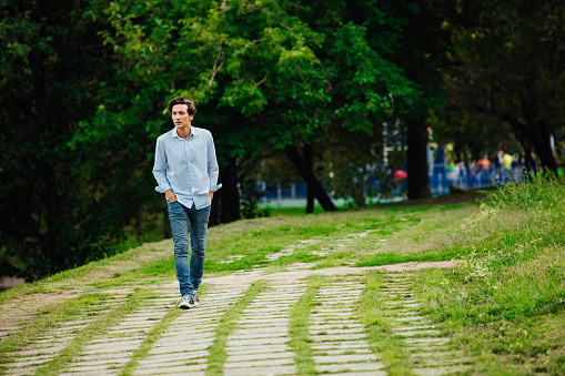 young adult in blue shirt and jeans walking alone in park