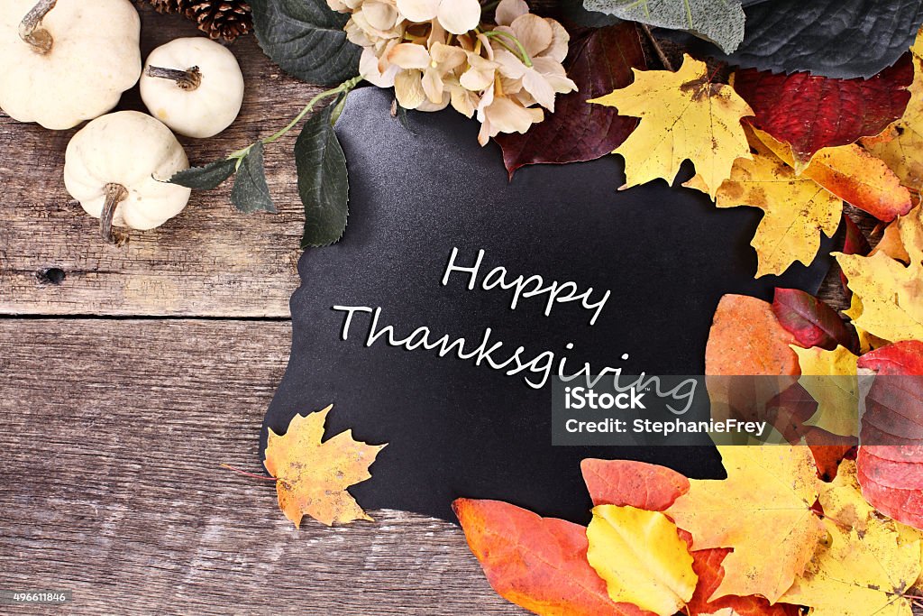 Fall Leaves Blackboard Chalk board with text Happy Thanksgiving surrounded by autumn leaves, flowers and white pumpkins over a rustic background. Autumn Stock Photo